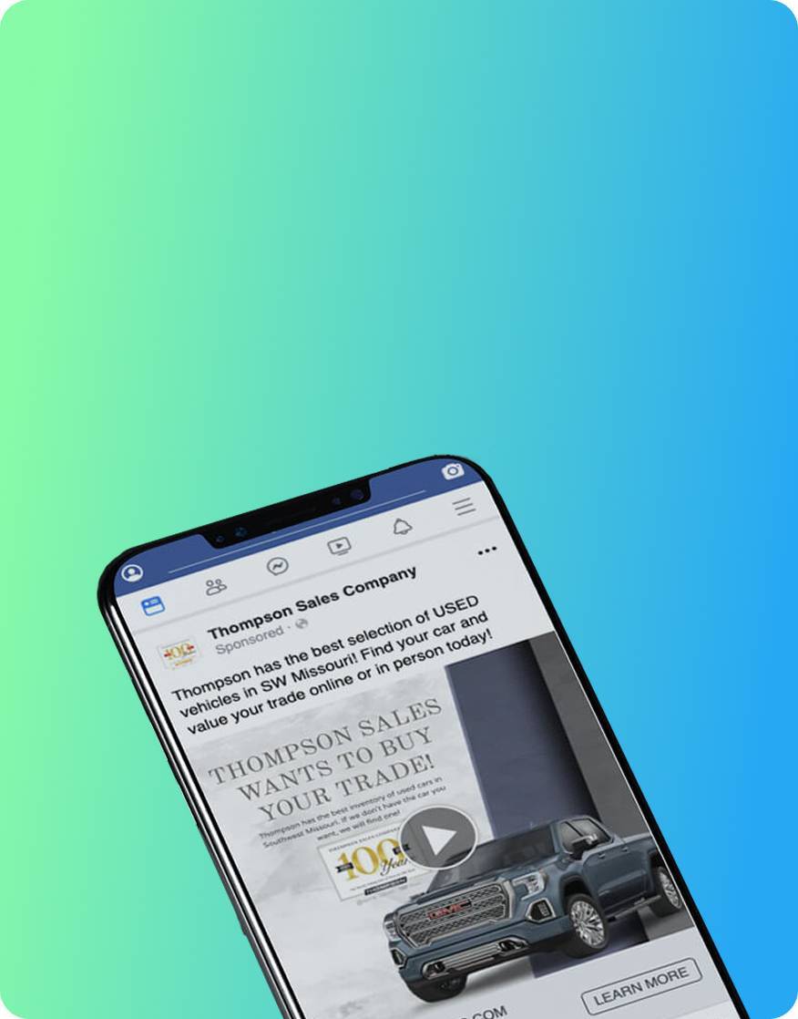 A smartphone displays a Facebook ad from Thompson Sales Company featuring a gray pickup truck and text promoting used vehicles and trade-in offers, set against a blue-to-green gradient background.
